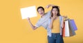 Asian couple holding blank billboard and shopping bags isolated on yellow background Royalty Free Stock Photo