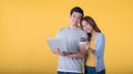 Asian couple holding credit card and laptop while looking at a camera isolated on yellow background