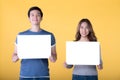 Asian couple holding empty blank boards and smiling at camera isolated on yellow background Royalty Free Stock Photo