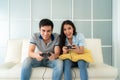 Asian couple man ans woman to playing video games with joysticks while sitting in sofa in living room at home, concept of family