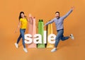 Asian Couple Near Giant Shopping Bags Jumping On Orange Background