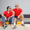 Asian couple resting after skateboarding. Young asian man in red T-shirt with collar and black sunglasses looking at his