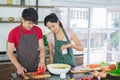 Asian couple`s in apron, make cooking together.  man are preparing to cut vegetables with knives. Woman mix salad dressing Royalty Free Stock Photo