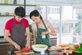 Asian couple`s in apron, make salads together.  man are preparing to cut vegetables with knives. Woman mix salad dressing Royalty Free Stock Photo