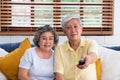 Asian couple senior sitting on sofa and use remote control to change channel and watching tv in living room at home Royalty Free Stock Photo
