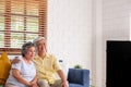 Asian couple senior sitting on sofa and  watching tv in living room at home.panning from blur foreground television Royalty Free Stock Photo