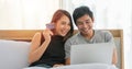 Asian Couple shopping online and paying with credit card at laptop computer,Happy couple at home surfing the net in bed Royalty Free Stock Photo