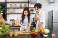 Asian couple spend time together in the kitchen. Young woman cutting green apple on a wooden chop board while her boyfriend stand Royalty Free Stock Photo