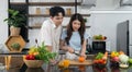 Asian couple spend time together in the kitchen. Young woman cutting orange fruit on a wooden chop board while her boyfriend stand Royalty Free Stock Photo