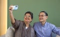 Asian couple spend time together in the living room. Retired woman and man take selfie photo with mobile phone. Modern lifestyle Royalty Free Stock Photo