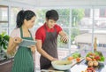 Asian couple are Standing cooking in the kitchen. Woman smile holding tablets. Men are picking vegetables in bowl prepare salad fo Royalty Free Stock Photo