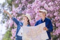 Asian couple tourist holding city map while walking in the park at cherry blossom tree during spring sakura flower festival Royalty Free Stock Photo