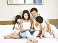 Asian couple and two children reading book together in bed Royalty Free Stock Photo