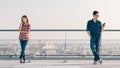 Asian couple using smartphone in distance on building rooftop. Coronavirus outbreak social distancing, new normal people lifestyle Royalty Free Stock Photo