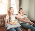 Asian couple watching movie sitting on a sofa at home cheerful and take popcorn to boy friend