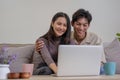 Asian couple watching movies on the internet using laptop at home Smiling Thai man and woman sitting on sofa, hugging Royalty Free Stock Photo
