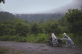 asian couples collaborated to push a malfunctioning motorcycle in the middle of the forest road