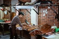 Asian craftsman in apron working with leather in workshop