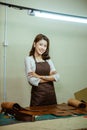 asian craftwoman wearing apron with crossed hands in tanned workspace