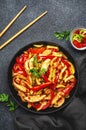 Asian cuisine, stir fry with chicken, red paprika pepper and zucchini in frying pan. Black kitchen table background, top view, Royalty Free Stock Photo