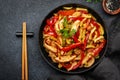 Asian cuisine, stir fry with chicken, red paprika pepper and zucchini in frying pan. Black kitchen table background, top view, Royalty Free Stock Photo