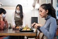 Asian customer woman dining in restaurant. Waitress with face mask serving food to customer sit on social distancing table for new