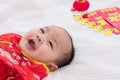 Asian cute baby boy Chinese Cheongsam costume toddler lie down on bed at home wiht gold ingots laughing good humored infant