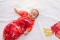 Asian cute baby boy Chinese Cheongsam costume toddler lie down on bed at home wiht gold ingots laughing good humored infant