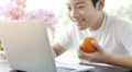 Asian cute boy using laptop computer and holding fresh orange Royalty Free Stock Photo