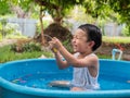 Asian cute child boy laughing while playing water in blue bowl with relaxing face and wet hair in rural nature. Royalty Free Stock Photo