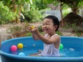 Asian cute child boy laughing while playing water in blue bowl with relaxing face and wet hair in rural nature Royalty Free Stock Photo