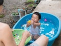 Asian cute child boy laughing while playing water in blue bowl with relaxing face and wet hair in rural nature. Royalty Free Stock Photo