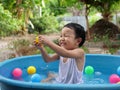 Asian cute child boy laughing while playing water in blue bowl with relaxing face and wet hair in rural nature. Royalty Free Stock Photo