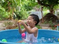 Asian cute child boy laughing while playing water in blue bowl with relaxing face and wet hair in rural nature. Royalty Free Stock Photo