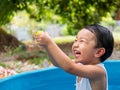 Asian cute child boy laughing while playing water in blue bowl with relaxing face and wet hair in rural nature. Royalty Free Stock Photo