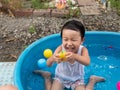 Asian cute child boy laughing while playing water in blue bowl with relaxing face and wet hair in rural nature. Royalty Free Stock Photo