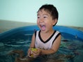 Asian cute child boy laughing while playing water in blue bowl with relaxing face and wet hair.