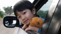 Asian cute child boy looking out car window with happy smiling face and hugging teddy bear with love. Royalty Free Stock Photo