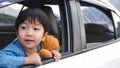 Asian cute child boy looking out car window with surprised face, hugging teddy bear with love in summer trip.