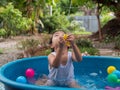 Asian cute child boy playing water in blue bowl with relaxing face and wet hair in rural nature. Royalty Free Stock Photo