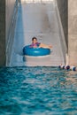 Asian cute child girl enjoying summer vacation, riding blue float ring sliding from water ramp to swimming pool, vertical image Royalty Free Stock Photo