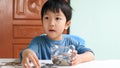 Asian cute child holding transparent piggy bank and looking with surprised face at home. Royalty Free Stock Photo