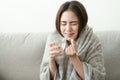 Asian Cute of  girl having headache and high temperature from illness holding pill of medicine and water sitting on sofa at home, Royalty Free Stock Photo