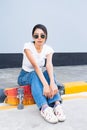 Asian cute girl or woman sit on street, place her legs on skateboard, and looking straight Ã¢â¬â¹in front of cool wall with copy