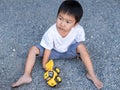 Asian cute little child boy playing yellow car toy outdoor with dirty foot