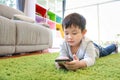 Asian cute and smart little boy lying on geen floor while using or playing game from cell phone device with attention face Royalty Free Stock Photo