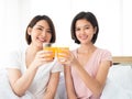 Asian cute two girls cheers glass of orange juice before drink together in the morning on white bed