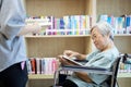 Asian daughter and senior mother reading a book in library from bookshelf,old wman with wheelchair,family enjoying, reading books, Royalty Free Stock Photo
