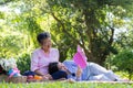Asian daughter Sleeping on mother lap and reading book on picnic mat in the park. A happy senior woman talks with her daughter. Royalty Free Stock Photo
