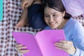 Asian daughter Sleeping on mother lap and reading book on picnic mat in the park. A happy senior woman talks with her daughter. Royalty Free Stock Photo